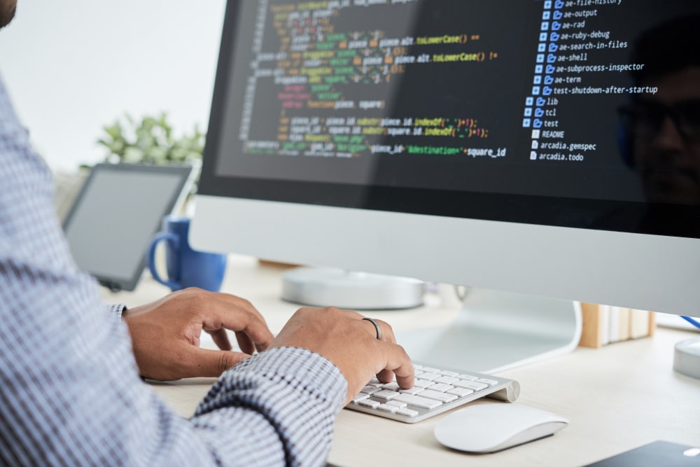 Photo représentant un homme qui rédige du code sur un écran d'ordinateur
