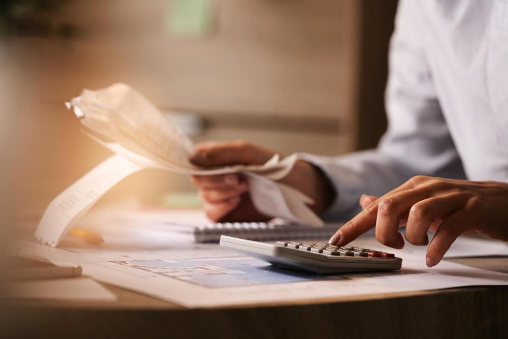 Mains d'une personne faisant de la comptabilité à l'aide d'une calculatrice tenant dans son autre main une liasse de reçus bancaires