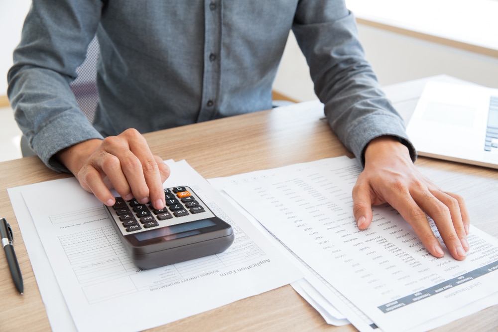 Homme assis à un bureau faisant les comptes à l'aide d'une calculatrice et d'un document de référence