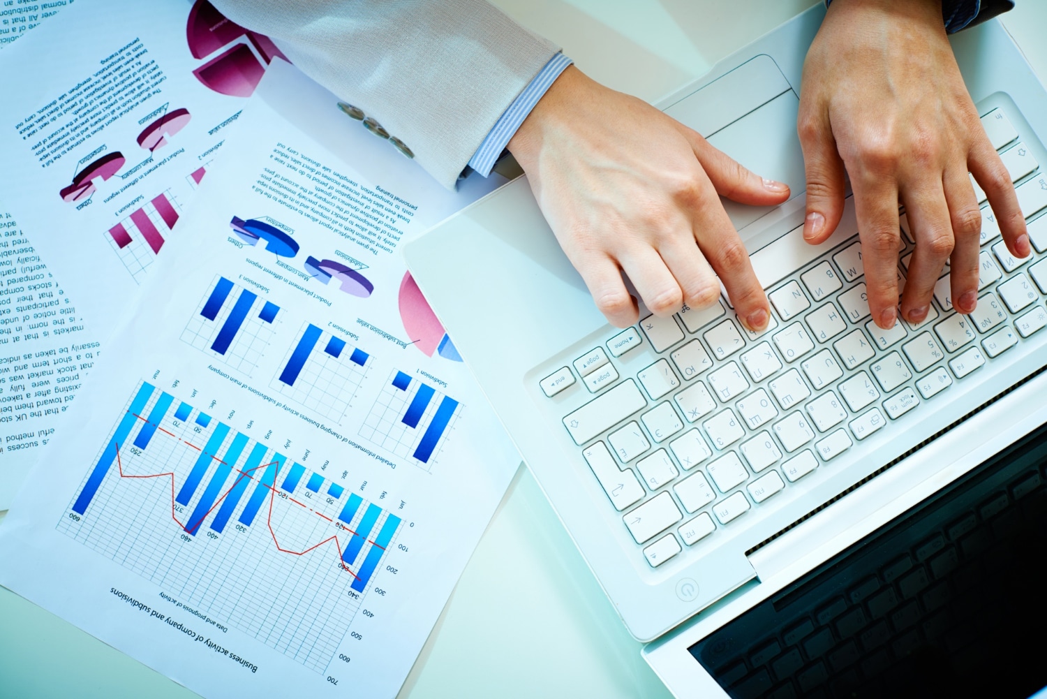 Point de vue du dessus d'un bureau avec un ordinateur portable et des fiches avec des statistiques imprimées. On voit également des mains qui écrivent sur le clavier de l'ordinateur.